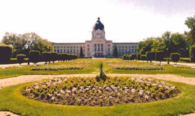 Vue générale de l'édifice de l'Assemblée législative, qui montre sa pelouse, ses massifs floraux, ses arbustes et ses arbres entourés et traversés d'allées de promenade et de routes, 1998. © Parks Canada Agency / Agence Parcs Canada, 1998.