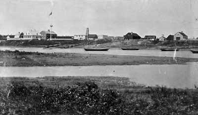 General view of Moose Factory, showing the Staff House at the left of the image, circa 1870. © Library and Archives Canada / Bibliothèque et Archives Canada, C-001718.