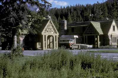 Vue latérale du bâtiment 3, qui montre le toit à pignon percé d’une  cheminée en pierres et revêtu de bardeaux de cèdre posés en quinconce pour créer un agencement irrégulier, 1985. © Parks Canada | Parcs Canada, 1985.