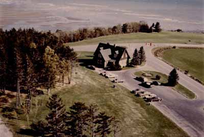 Bird's eye view of the Visitor Information Centre East, showing the building’s picturesque design and location in an open setting which in turn emphasizes the rustic nature of the setting, c. 1980. © Parks Canada Agency / Agence Parcs Canada, c./vers 1980.
