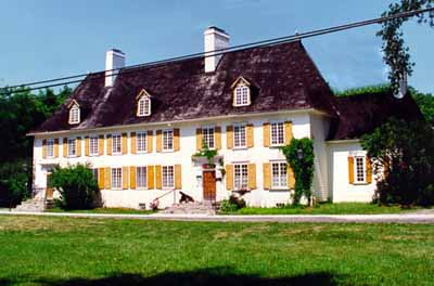 General view of Mauvide-Genest Manor, showing the substantial two-storey rectangular massing of the manor’s main block under a steeply hipped roof broken by small dormer windows and two large chimneys. © Parks Canada Agency / Agence Parcs Canada.