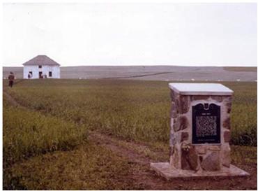 La plaque de Fort Pitt érigé par la province de Saskatchewan en 1973 avec la reconstruction de la maison du facteur en chef à l’arrière plan. © Parks Canada / Parcs Canada,