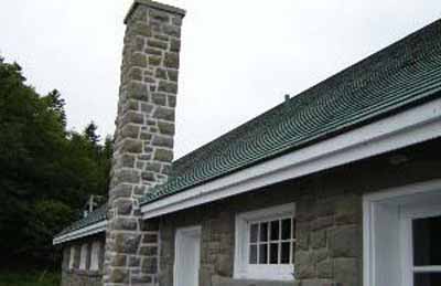View of the exterior of the Bathhouse, showing the exterior materials and finishes, particularly the rough-cut, irregularly coursed stone, wood trim, and cedar roof shingles. © Parks Canada Agency / Agence Parcs Canada.