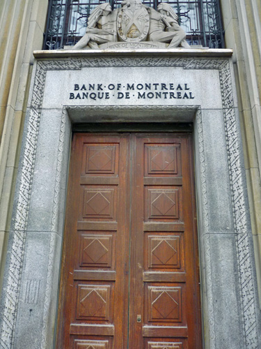 Vue générale de la Banque de Montréal , montrant son entrée centrale ornée d’une moulure sculptée et surmontée d’une sculpture des armoiries de la banque, 2011. © Parks Canada Agency / Agence Parcs Canada, M. Therrien, 2011.
