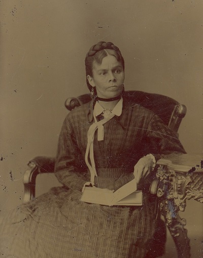 1961.027.057 Nahneebahweequay (Catharine Sutton), no date (seated, book
in lap, white ribbon at neck) (© The Grey Roots Archival Collection | Collection archivistique de Grey Roots)