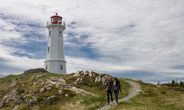 Two people walking on a path by a lighthouse.