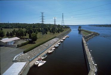 Navigation channel downstream of the lock. To the left, many boats waiting the next lockage upstream on the dock. Distant scene of the Carillon park.