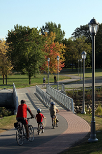 Several site visitors biking along the beautiful bike paths , crossing a bridge that covers the Lairet River in Cartier-Brébeuf National Historic Site.