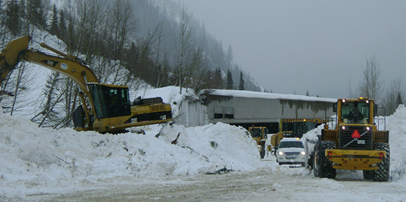 Parks Canada highway crews clean up avalanche debris covering the road.