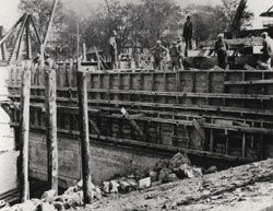 Treize ouvriers sur le coffrage de bois qui retient le béton, lors de la construction de l'écluse actuelle du canal de Saint-Ours en 1931. 