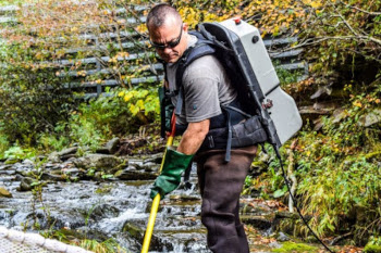 Kurt Samways, titulaire de la chaire de recherche, se tient dans un petit ruisseau, un appareil de pêche électrique sur le dos.