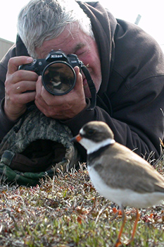 Un homme allongé sur le sol prend une photo d’un oiseau.