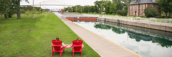 Two red chairs beside a canal.