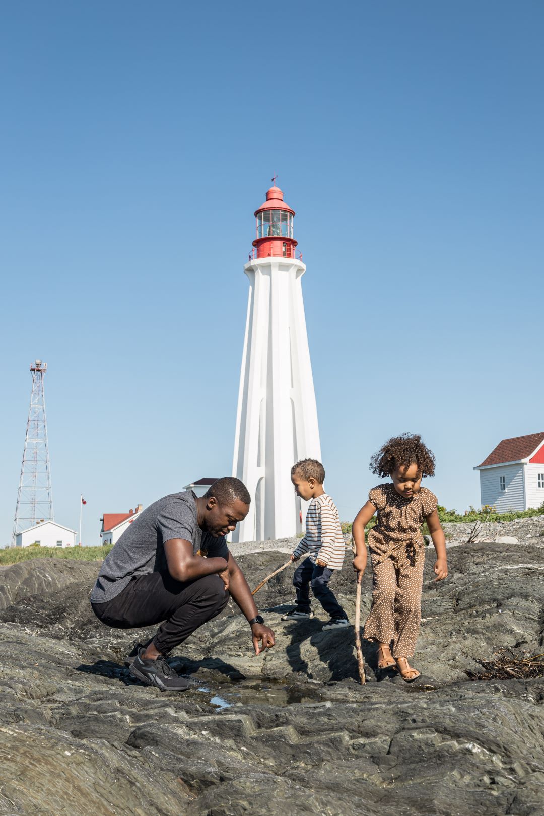 A family plays on the shore with a lighthouse in the back.