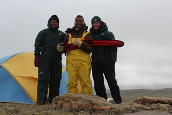 Three people standing before a tent on the tundra.