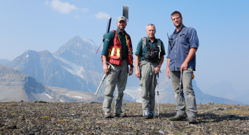 Three men standing against a backdrop of mountains.