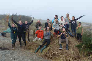 Volunteers and park staff raise their arms while sitting on a pile of invasive plants that they have removed from Sidney Island.