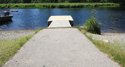 An asphalt path leads to a floating river dock with plastic docking platform and a wooden section.