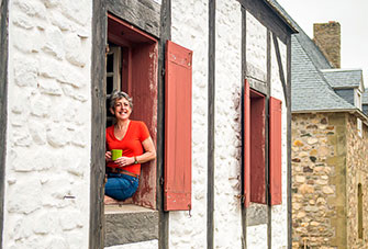 A woman drinks coffee as she sits on the window sill of a period building located in the heart of a fortified town. 