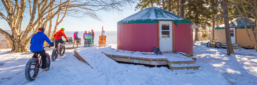 A group of friends with fat bikes, snowshoes and skis near two yurts on the Bay of Fundy shore on a sunny winter day.