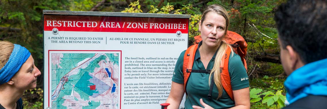 A Parks Canada guide discusses the restricted area with hikers, green foliage in the background.