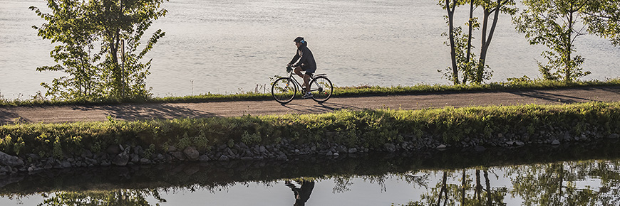A person is cycling on the Chambly Canal’s path along the water
