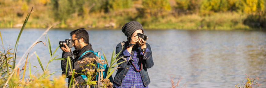 Two photographers take wildlife photos by a lake.