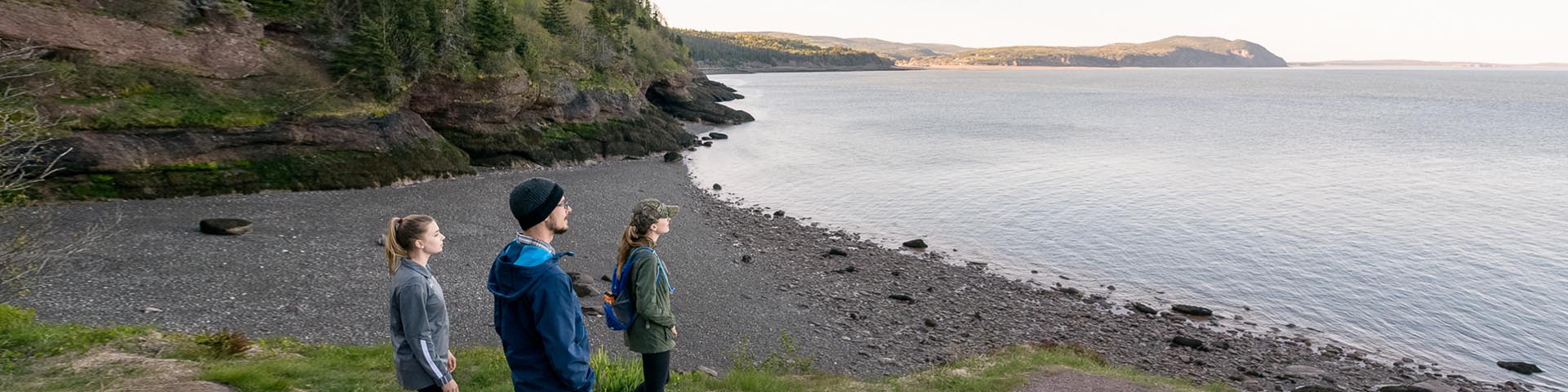 Trois visiteurs du parc se tenant sur une falaise maritime face à la baie de Fundy.